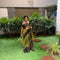 A woman wearing a navy blue and red patterned saree stands in a garden courtyard in front of a small white and red deity shrine.