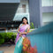 A woman wearing a navy blue and red patterned saree stands in a garden courtyard in front of a small white and red deity shrine.