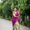 A woman wearing a navy blue and red patterned saree stands in a garden courtyard in front of a small white and red deity shrine.