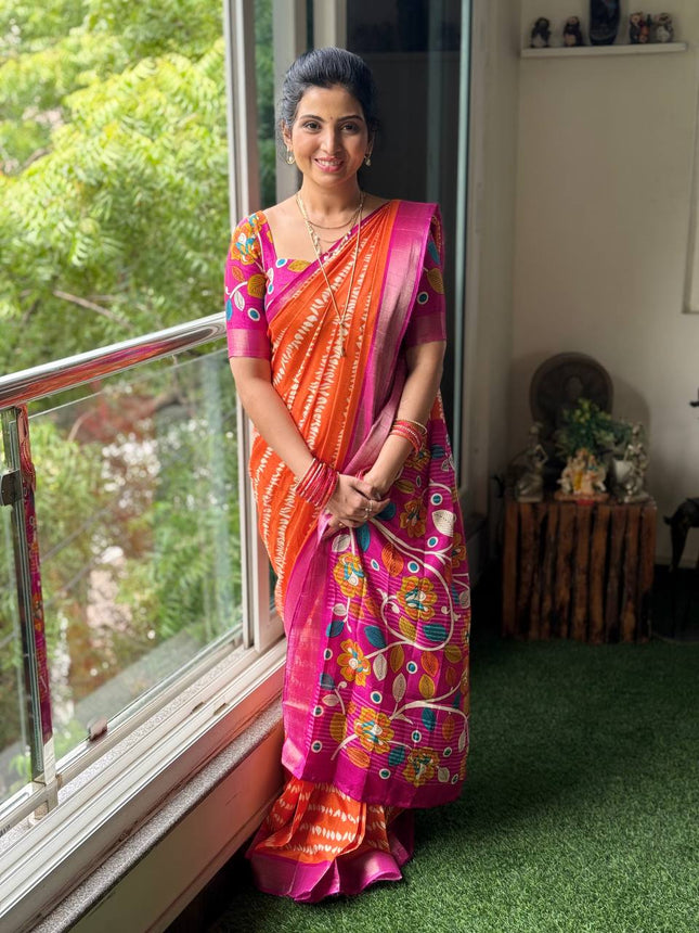 Woman in a colorful saree standing by a window with greenery outside