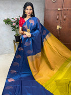 A woman showcasing a blue and yellow saree with a floral design, presented by LAKSHMI BOUTIQUE.