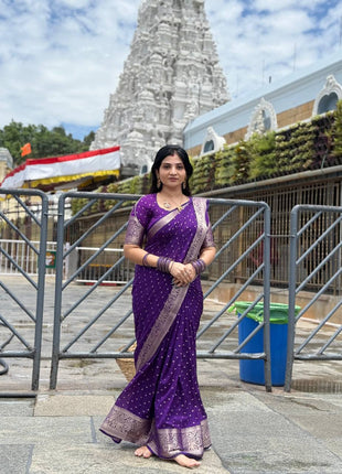 Woman in a purple saree standing in front of a temple structure.