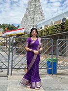 Woman in a purple saree standing in front of a temple structure.