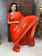 Woman in a red saree sitting on a decorative chair.